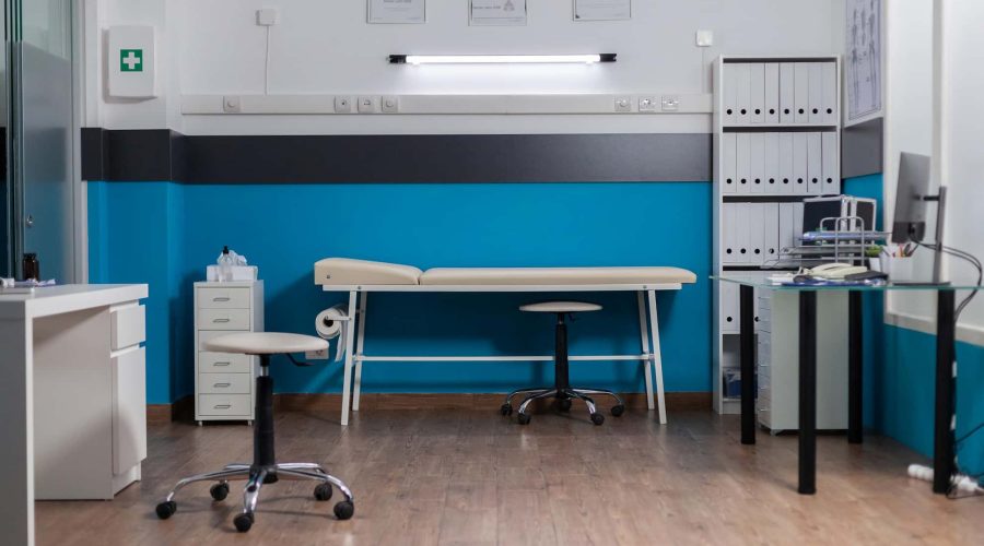 Une salle d'examen médical propre et moderne avec des couleurs bleu et blanc, une table d'examen, des chaises de bureau, des armoires et des étagères avec des classeurs.