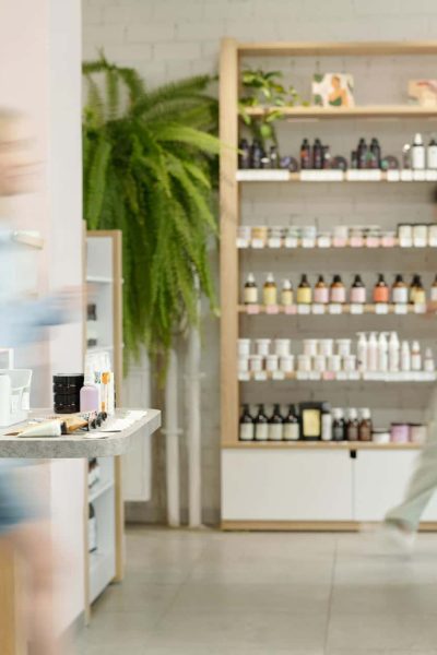 Deux personnes marchent à l'intérieur d'un magasin bien éclairé dont les rayons présentent divers produits de soin et de beauté.