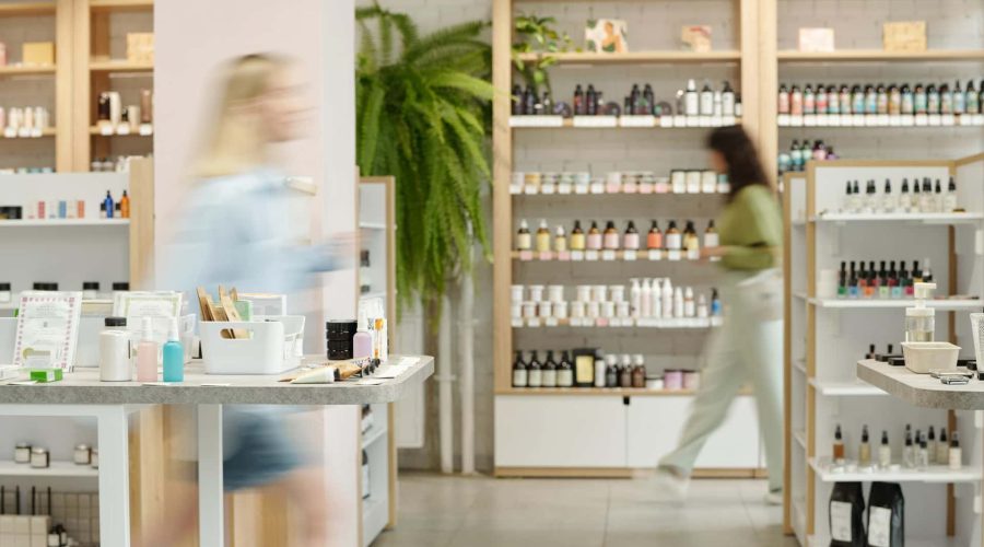 Deux personnes marchent à l'intérieur d'un magasin bien éclairé dont les rayons présentent divers produits de soin et de beauté.