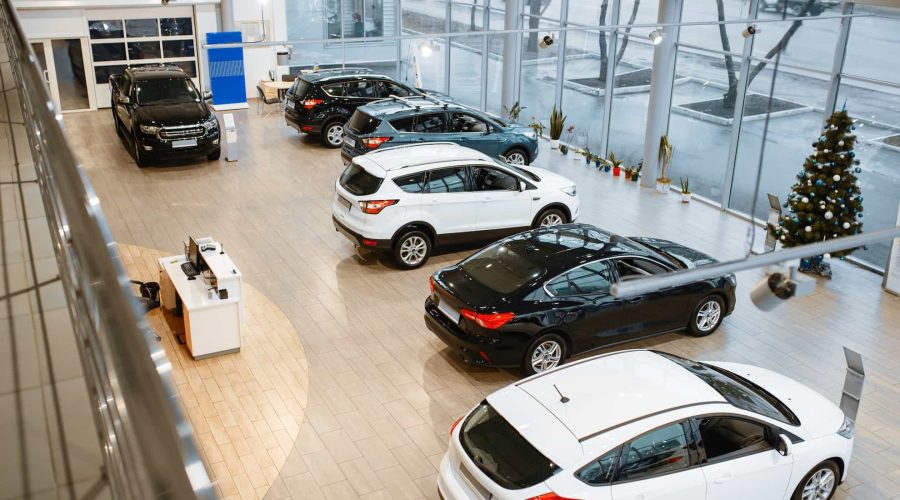 Vue large d'une salle d'exposition moderne d'un concessionnaire automobile présentant plusieurs voitures neuves, avec de grandes fenêtres, un bureau de réception et un arbre de Noël décoré.