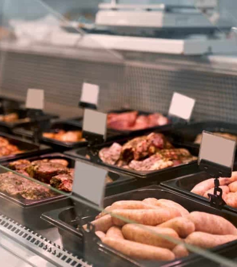 Dans une boucherie, une vitrine contenant différents types de viandes crues et de saucisses soigneusement rangées dans des plateaux, chacun portant une étiquette de prix vierge, témoigne du niveau d'organisation d'un agencement de bureau.