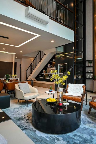 Salon moderne à aire ouverte avec mobilier contemporain, table basse en verre, plantes décoratives et escalier menant à l'étage supérieur. Tons neutres, éclairage d'appoint et grandes fenêtres.