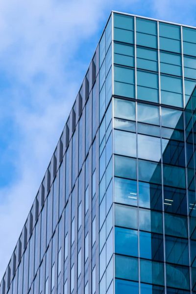 Immeuble de bureaux moderne en verre avec des fenêtres réfléchissantes sur fond de ciel bleu avec des nuages.