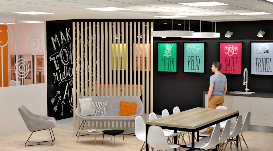 Salon de bureau moderne avec des affiches colorées sur un mur noir, une cloison en lattes de bois, un canapé, des chaises, une table et une personne debout près d'un évier et d'un réfrigérateur orange.