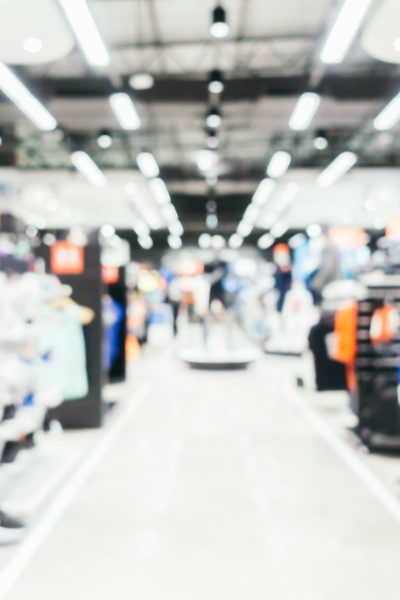 Image floue de l'intérieur d'un magasin de vêtements avec des mannequins et des étagères de vêtements visibles sous les lumières du plafond.