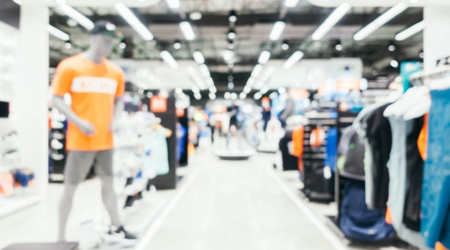Image floue de l'intérieur d'un magasin de vêtements avec des mannequins et des étagères de vêtements visibles sous les lumières du plafond.