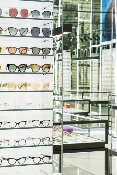 Étagères remplies de montures de lunettes de différents styles et couleurs dans un magasin d'optique bien éclairé.