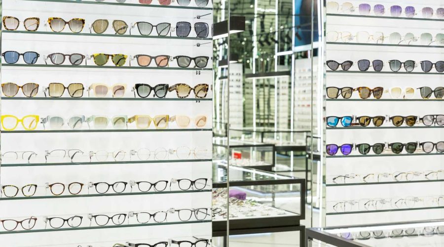 Étagères remplies de montures de lunettes de différents styles et couleurs dans un magasin d'optique bien éclairé.