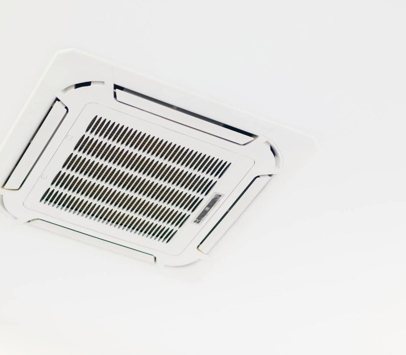 Une bouche d'air conditionné blanche montée au plafond avec un motif de grille au centre d'un plafond blanc.