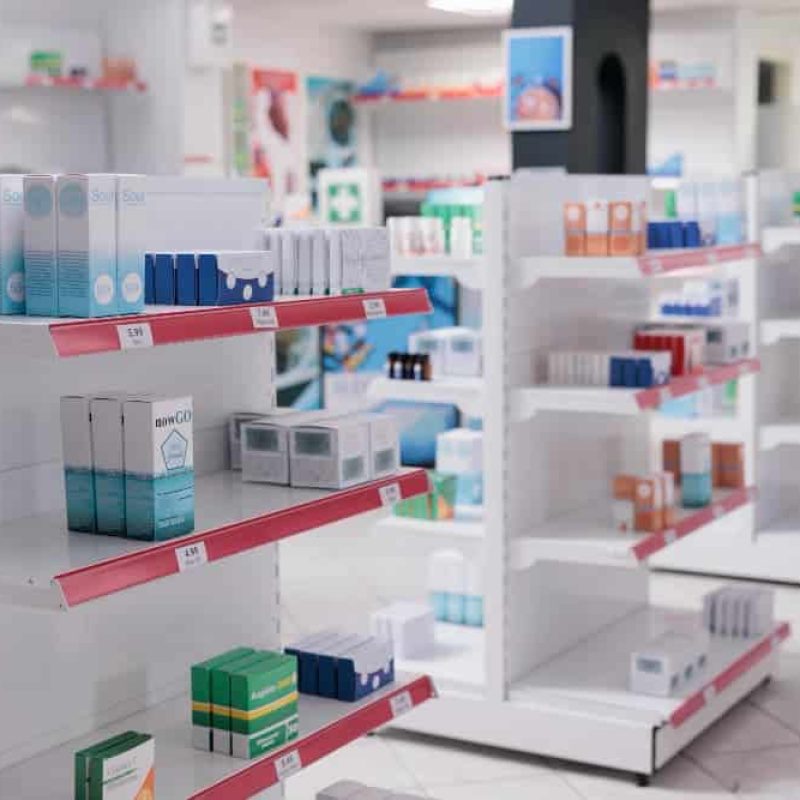 Les rayons d'une pharmacie ou d'une droguerie, conçus avec soin agencement de bureau, sont garnis de diverses boîtes de médicaments et de produits de santé, soigneusement disposées en rangées sur des présentoirs blancs.