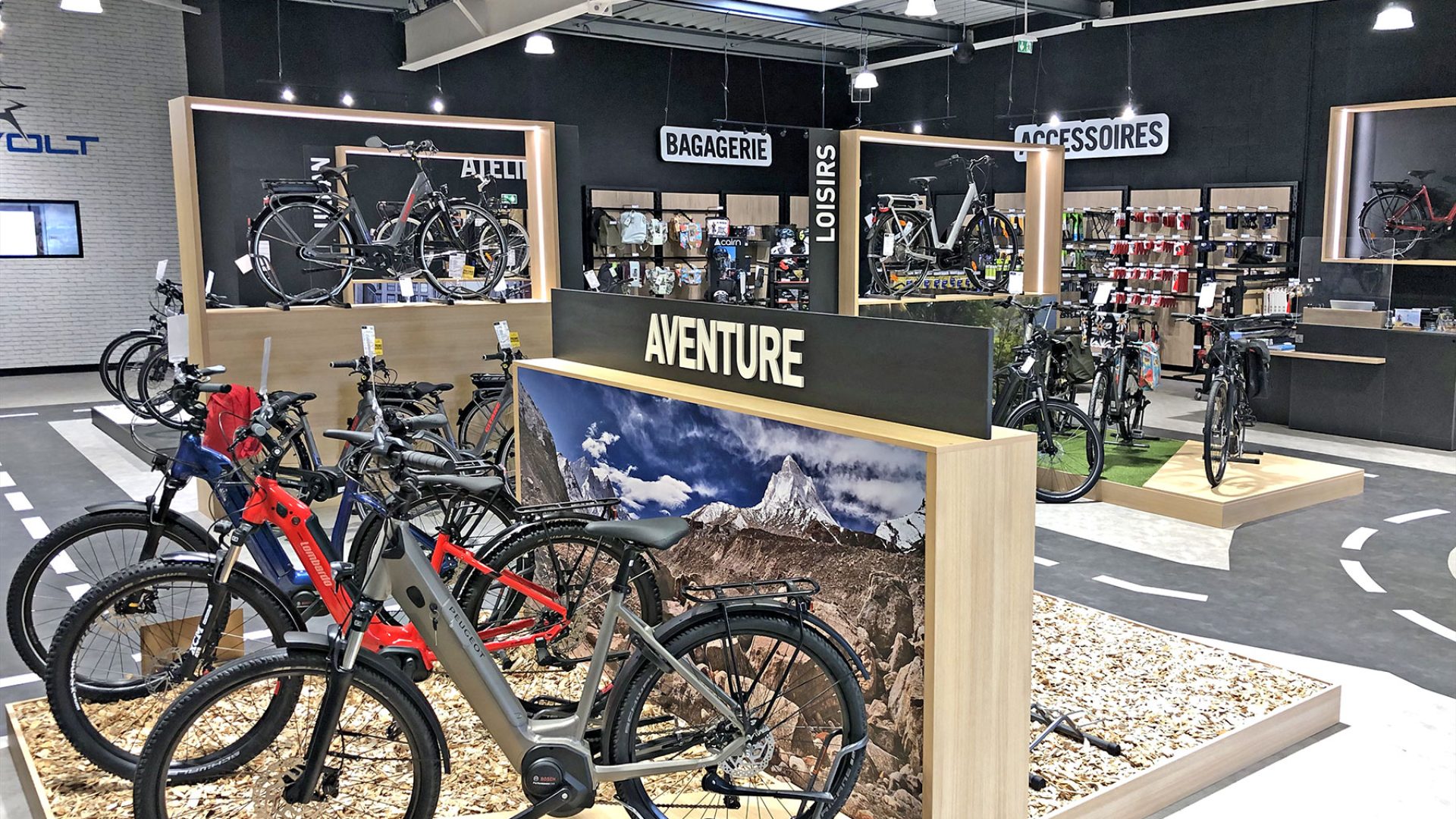 L'intérieur d'un magasin de vélos moderne présente divers vélos, accessoires et équipements sur des racks et des étagères, avec des panneaux en français indiquant les différentes sections.