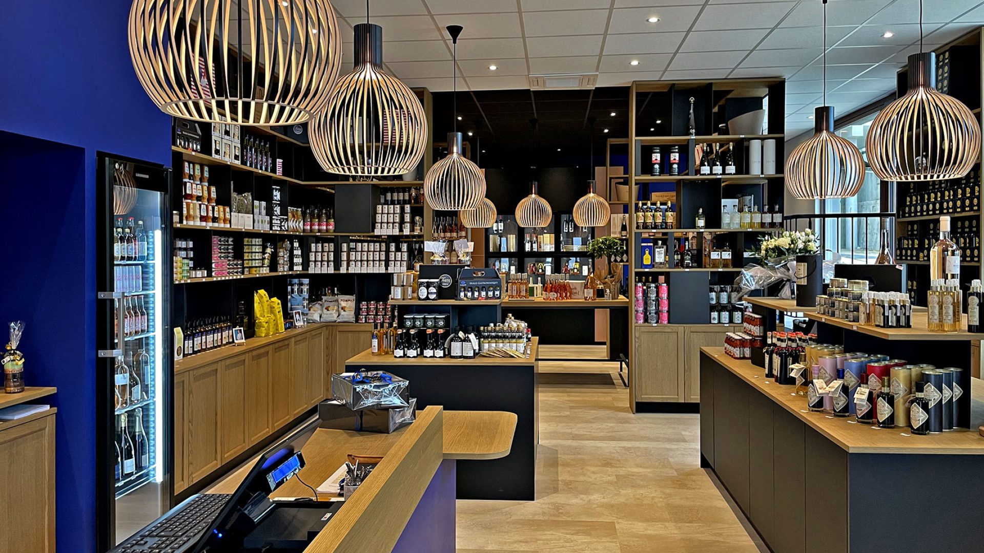 Intérieur d'une épicerie fine moderne avec des étagères en bois, des lampes suspendues et divers produits emballés présentés dans l'espace.
