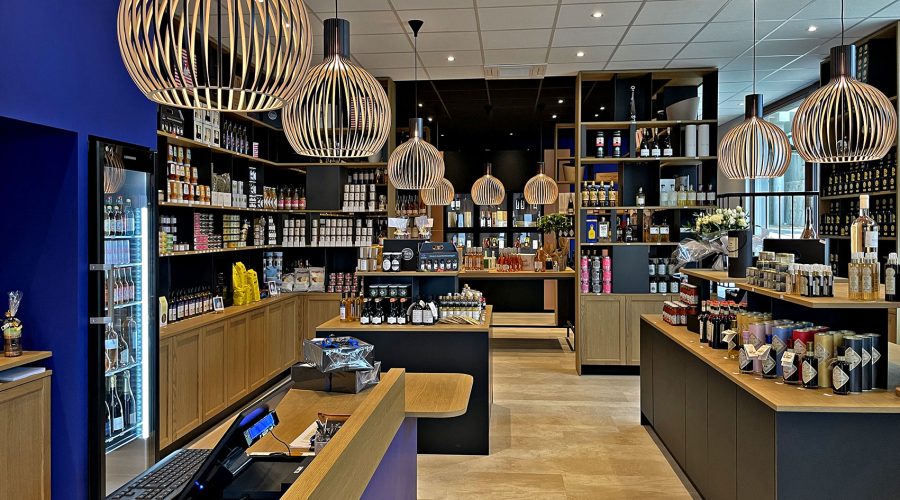 Intérieur d'une épicerie fine moderne avec des étagères en bois et des lampes suspendues, présentant divers aliments emballés, des bocaux et des bouteilles soigneusement disposés dans le magasin.