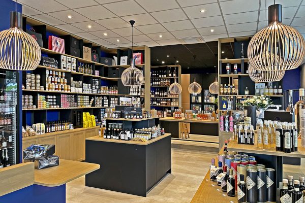 L'intérieur d'une épicerie fine moderne avec des étagères remplies d'aliments spécialisés, de vins et de condiments sous des lampes suspendues contemporaines.
