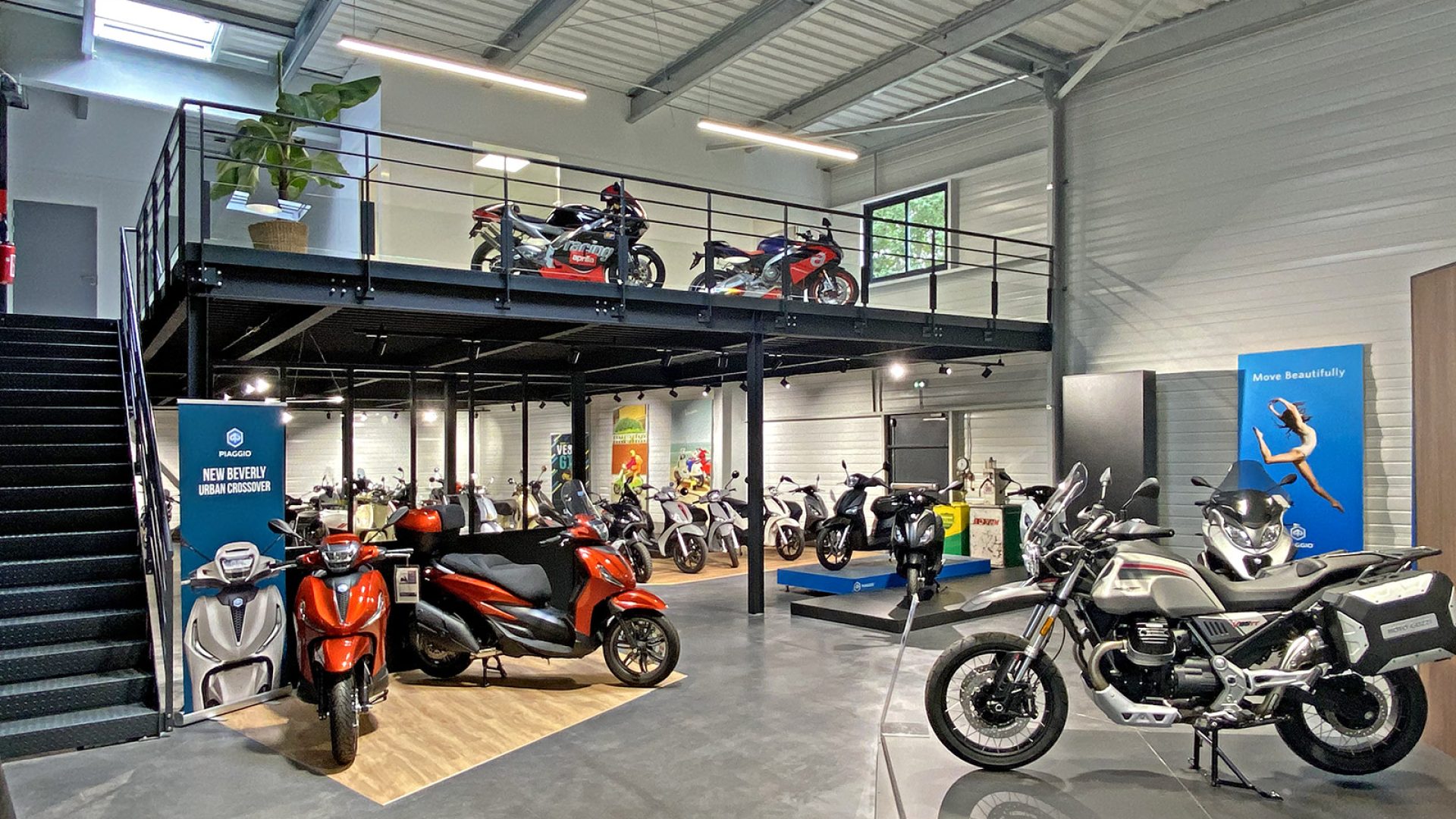 Une salle d'exposition de motos moderne avec différents modèles exposés, y compris des scooters et des motos de tourisme, au rez-de-chaussée et au niveau de la mezzanine.