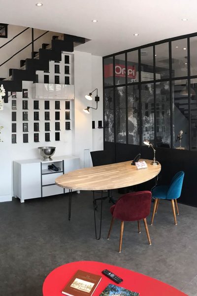 Espace de bureau moderne avec un escalier, une salle de réunion vitrée, une table ronde en bois avec des chaises colorées et divers éléments décoratifs.